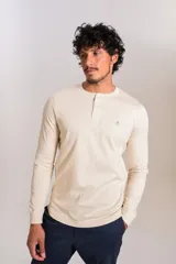 Remera de manga larga tipo Henley color beige, con cuello redondo y cierre frontal parcial con botones. Presenta un pequeño logo bordado en el pecho.