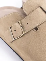 Zuecos cerrados al frente color negro, confeccionados en material símil gamuza. Presentan una tira ajustable con hebilla metálica en el empeine y una suela con detalle de corcho en el talón.