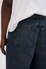 Jean de cinco bolsillos en denim de algodón grueso, color azul oscuro con efecto lavado. Modelo de corte holgado de cadera a bajo con pierna redondeada ancha y tiro bajo. Cintura estándar con cierre de botón y cremallera.