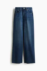 Jean de tiro alto con corte wide leg, confeccionado en denim rígido de lavado azul clásico. Presenta diseño de cinco bolsillos, cierre frontal con botón y ruedo desflecado.
