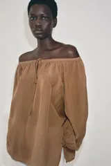 Blusa de lino color amarillo pastel, con escote recto ajustable mediante lazadas, hombros descubiertos y mangas largas abullonadas con puños elásticos.