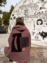 Campera tipo hoodie de textura bouclé en color chocolate, con diseño de collage en la espalda que incluye un aplique de gamuza oscura y un parche con textura de piel de serpiente. Presenta capucha y un pequeño parche de cuero sintético con logo en la parte inferior.