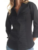 Camisa entallada de color negro con pechera estructurada mediante alforzas horizontales. Presenta cuello con solapa, escote en V, cierre frontal con botones y mangas tres cuartos con puños anchos rebatibles.