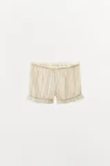 Shorts de tiro medio y cintura elástica ajustable con cordones, confeccionados en tejido plumeti con detalles de frunces y terminaciones con volados en el bajo.