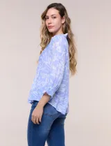 Blusa celeste con estampado efecto pincelada blanca, de corte semi holgado, escote en V con cuello solapa y media abotonadura frontal con botones nacarados. Presenta finas alforzas verticales en la pechera y mangas 3/4 con puños elastizados.