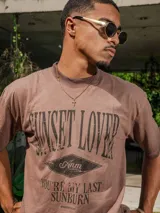 Remera de jersey con efecto teñido, color marrón, de corte holgado y cuello redondo. Presenta un estampado frontal con texto en tonos más oscuros.