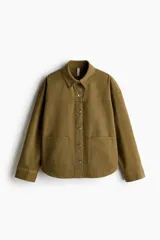 Campera camisera de sarga de algodón color verde militar, con cuello clásico, cierre frontal de botones metálicos, canesú y bolsillos de parche delanteros.