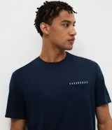 Pijama corto masculino confeccionado en mezcla de algodón, viscosa y elastano. Incluye una remera de manga corta, cuello redondo y bolsillo frontal con detalle listrado, combinada con un short de rayas finas y cintura elástica.