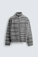 Chaqueta de punto con diseño de rayas horizontales en tonos grises, cuello subido y cierre frontal de cremallera completa. Presenta un corte relajado y acabados en rib en puños y bajo.