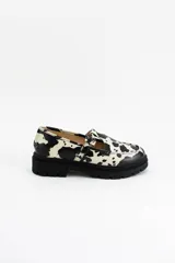Mocasines estilo Mary Jane con diseño de estampado de vaca (cow print), confeccionados en cuero. Presentan una tira con hebilla ajustable sobre el empeine y una suela track negra de 4,5 cm de altura.