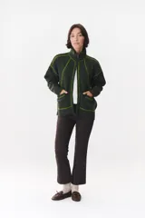 Campera de tejido de punto color marrón con destellos de lurex, corte oversize y cierre frontal. Presenta detalles de costuras y terminaciones en color crema, cuello alto y bolsillos frontales.