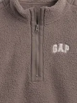 Buzo de polar tipo sherpa color marrón, con cuello alto y cierre frontal parcial. Presenta el logo de la marca bordado en el pecho y detalles de costuras reforzadas en hombros y mangas.