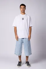 Remera oversize de corte holgado, color blanco, con cuello redondo y mangas cortas. Presenta un pequeño estampado circular en el centro del pecho con un diseño abstracto inspirado en arrecifes.