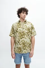 Camisa de manga corta con cuello camisero y estampado de hojas en tonos verde oliva y beige sobre fondo claro.