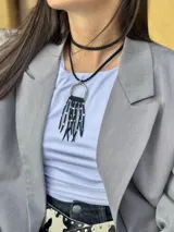 Collar corto con dije de flecos negros y cuentas plateadas, colgando de un aro metálico plateado. El collar es de tiento trenzado negro y tiene un choker negro liso.
