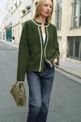 Chaqueta de punto color verde oscuro con cuello redondo y cierre frontal de botones. Presenta detalles de vivos en color crema en el cuello, la tapeta de botones y los puños.
