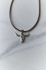 Collar con dije de acero quirúrgico en forma de cráneo de toro, montado sobre un cordón marrón.