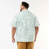 Camisa de manga corta verde claro y blanca con estampado tropical de hojas, cuello camisero, cierre frontal con botones y bolsillo aplicado en el pecho.