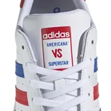 Championes Adidas Superstar blancos con detalles en azul y rojo. Presentan las tres tiras características de Adidas en los laterales en azul y rojo, y refuerzo de talón en rojo con la palabra "STAR" en blanco. La puntera es de goma con textura.