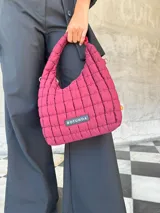 Cartera tipo hobo de diseño acolchado con costuras cuadradas, color bordó. Cuenta con un asa superior fija y un detalle de eslabones decorativos en un lateral. Incluye etiqueta con logo de la marca en la parte frontal.