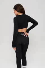 Conjunto deportivo de tres piezas en color negro, compuesto por un top de manga larga con cuello redondo y logo estampado, un top de bretel ancho y una calza chupín de tiro alto. El diseño presenta detalles de tejido con textura en zonas estratégicas.