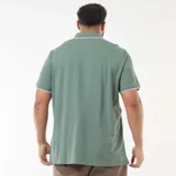 Remera tipo polo de manga corta en color verde, con detalles de ribete blanco en el cuello y en los bordes de las mangas. Presenta cierre frontal con tres botones y un pequeño logo bordado en el pecho.