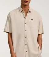 Camisa de corte relajado para hombre, confeccionada en una mezcla de cáñamo y algodón. Presenta cuello inglés, manga corta, cierre frontal con botones y un bolsillo en el pecho con una pequeña etiqueta aplicada.