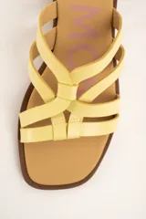 Sandalias planas de cuero color amarillo, con múltiples tiras finas entrelazadas en el empeine, suela baja y plantilla marrón.