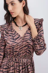 Vestido corto con estampado de cebra en tonos marrón y negro. Presenta mangas largas con puños elásticos, volados en los hombros y cintura elástica con lazo ajustable. Tiene tachas metálicas termo adhesivas en el escote y hombros.