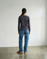 Remera de manga larga en jersey con estampado de líneas orgánicas en tonos verdes, violetas y naranjas. Presenta un corte recto y cuello redondo, diseñada para un ajuste cómodo y versátil.