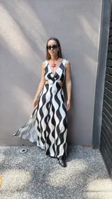 Vestido largo de tela sedosa con estampado de ondas verticales en blanco y negro, escote en V, cut out en la cintura, espalda regulable con lazo y elástico, y tajos laterales.
