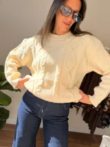 Sweater de tejido de punto grueso color crema, con diseño de trenzas en relieve, cuello redondo, mangas largas y terminaciones acanaladas en puños, cuello y cintura.