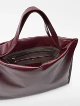 Maxi shopper de diseño minimalista con acabado brillante y textura craquelada. Cuenta con un compartimento principal con cierre magnético, bolsillo interior con cremallera y asas de hombro integradas. Logo de la marca grabado en la parte inferior frontal.
