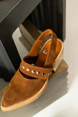 Zapato marrón de gamuza con taco de madera, punta fina y tira con apliques metálicos.