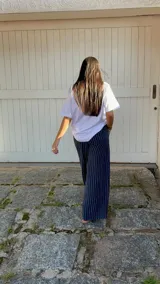 Pantalón de corte ancho y relajado, confeccionado en lino con diseño de rayas verticales. Presenta cintura elástica con cordón de ajuste y bolsillos laterales.