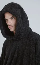 Hoodie oversize tipo anorak confeccionado en piel sintética de corderito, color negro. Presenta cierre central parcial, capucha ajustable con cordones y bolsillo canguro frontal.