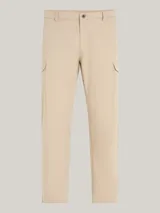 Pantalón cargo beige de corte amplio con pierna cónica, confeccionado en tejido elástico con propiedades antiarrugas y antiolores. Cuenta con cierre de cremallera y botón, dos bolsillos laterales abiertos, dos bolsillos laterales tipo cargo y dos bolsillos traseros de ojal. Logo de Tommy Hilfiger bordado en la parte trasera.