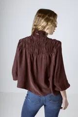 Blusa negra de manga larga con cuello alto fruncido y diseño amplio con frunces en la parte superior.