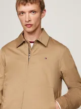 Campera Tommy Hilfiger modelo Ivy, color beige, de corte regular, confeccionada en algodón. Tiene cuello inglés, cierre de cremallera, dos bolsillos diagonales en la cintura, puños con botón y logo de la marca bordado en el pecho.