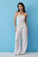 Blusa strapless blanca de corte asimétrico con terminación en punta y flecos sutiles en el borde inferior. Presenta escote palabra de honor y diseño recto.