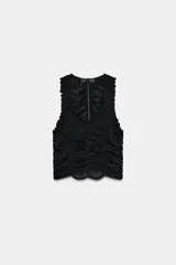Top negro sin mangas con escote pico profundo y detalle de frunces o drapeado en todo el frente. El ruedo inferior tiene un borde festoneado.