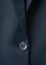 Blazer negro de corte recto con solapas de muesca, cierre frontal de un botón, bolsillos con solapa en los laterales y un bolsillo de ribete en el pecho.