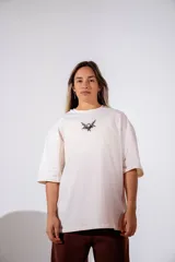 Remera de corte oversize color blanco, con cuello redondo y mangas cortas. Presenta un pequeño estampado gráfico central en el pecho con diseño de querubín con alas.
