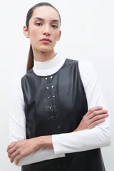 Minivestido negro de cuero ecológico con cuello redondo y sin mangas. Presenta tachas plateadas en el frente y cierre trasero.