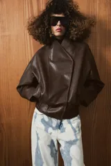 Chaqueta bomber de efecto piel en color marrón oscuro, con cuello subido, cierre frontal cruzado con botones a presión, bolsillos laterales y bajo elástico.
