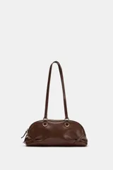 Bolso de hombro de color marrón, con diseño alargado y detalle de anillas metálicas doradas en la base de las asas. Cuenta con cierre de cremallera superior y doble asa fina para llevar colgado.