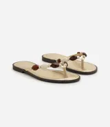 Sandalias planas tipo mule de dedo de la marca Satinato, en color dorado con plantilla metalizada y suela baja. Presenta una tira con aplicaciones decorativas de cuentas de resina en tonos marrones y marfil.
