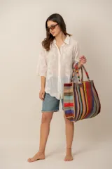 Bolso de hombro tipo tote grande, confeccionado con tejido de yute o fibras naturales con diseño de rayas verticales multicolor en tonos tierra, azul, verde, amarillo, rojo y naranja, con asas dobles fijas.