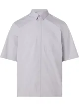 Camisa de manga corta color gris claro, corte boxy, cuello en punta, bolsillo de parche en el pecho y logo monograma de Calvin Klein estampado.