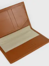 Porta pasaporte de cuero color marrón tostado, de diseño vertical y minimalista con costuras pespunteadas a contratono. Presenta el logotipo de la marca grabado en la esquina inferior y sello interior con la leyenda de autenticidad.